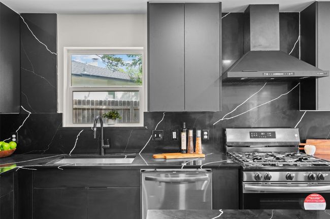 Kitchen featuring wall chimney exhaust hood, appliances with stainless steel finishes, modern cabinets, and a sink | Image 9
