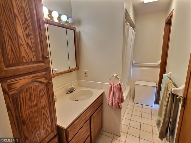 The main level bathroom offers a shower/tub combo, tile floors, and a linen closet. | Image 14