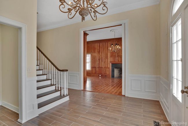 Foyer entrance with a chandelier, ornamental molding, stairs, a decorative wall, and wood finished floors | Image 7