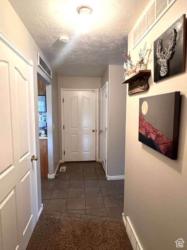 Corridor featuring visible vents, baseboards, dark tile patterned flooring, and a textured ceiling | Image 6