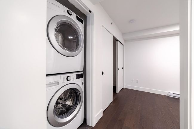 Laundry room with estacked washer and dryer, dark wood-style floors, and a baseboard heating unit | Image 33