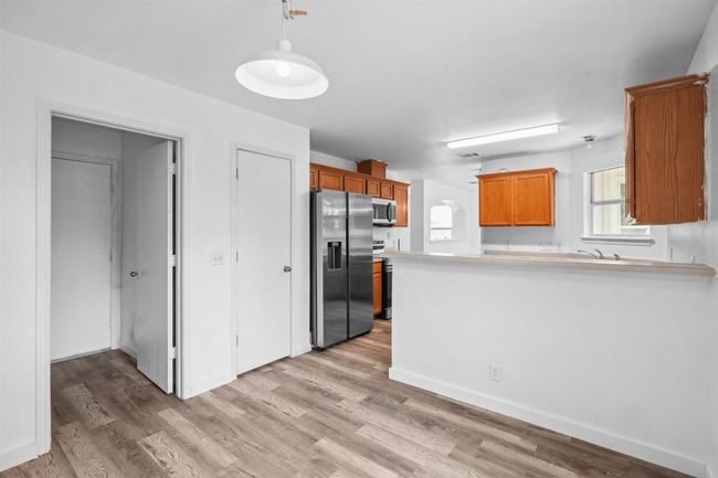 Kitchen featuring brown cabinetry, appliances with stainless steel finishes, hanging light fixtures, a peninsula, and light wood-style floors | Image 12