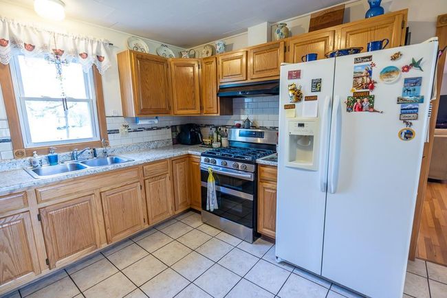 Kitchen with white fridge with ice dispenser, stainless steel gas range oven, sink, and tasteful backsplash | Image 5