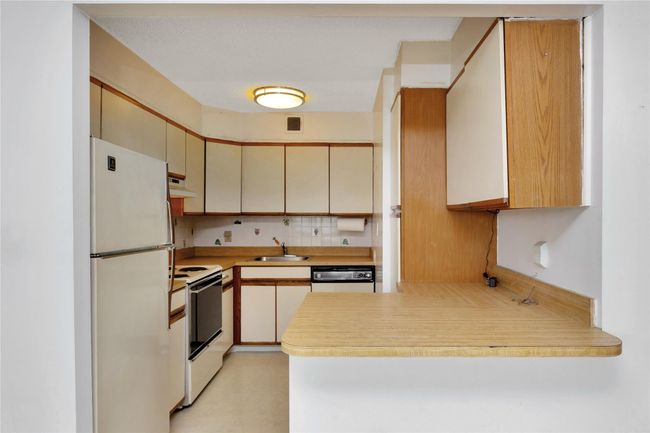 Kitchen with white appliances, under cabinet range hood, a peninsula, light countertops, and cream cabinetry | Image 5