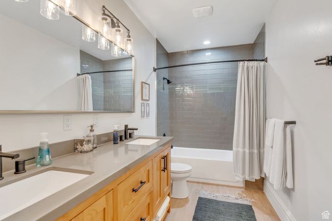 Full bathroom featuring double vanity, shower / bath combo with shower curtain, and wood finished floors | Image 56