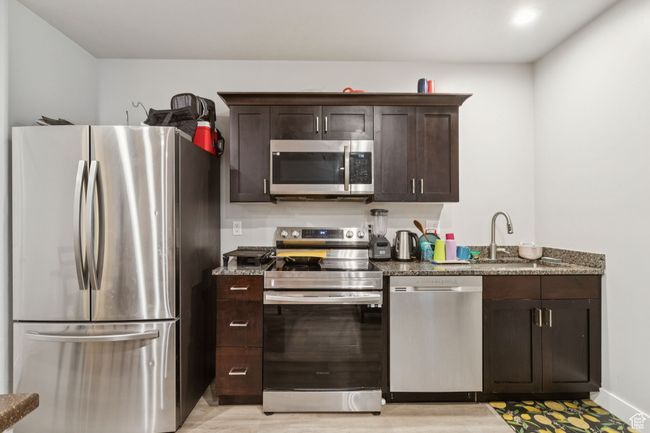 Kitchen with stainless steel appliances, dark brown cabinets, dark stone counters, and light wood-style floors | Image 34