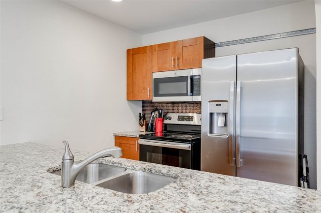 Kitchen with appliances with stainless steel finishes, brown cabinets, backsplash, and light stone countertops | Image 11