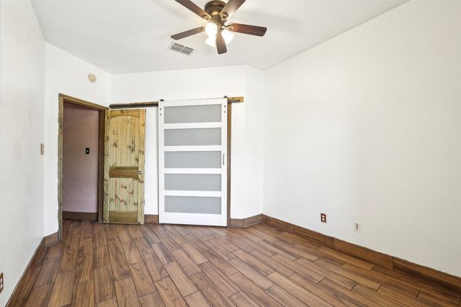 Unfurnished bedroom featuring dark wood-style floors, a barn door, baseboards, and ceiling fan | Image 19
