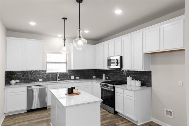 Kitchen with white cabinets, wood finished floors, a sink, and stainless steel appliances | Image 16