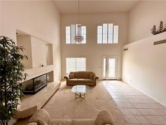 Living area with a towering ceiling, tile patterned flooring, a tile fireplace, and a chandelier | Image 4