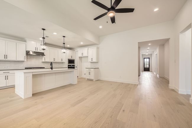 Kitchen featuring under cabinet range hood, black oven, tasteful backsplash, a ceiling fan, and recessed lighting | Image 7