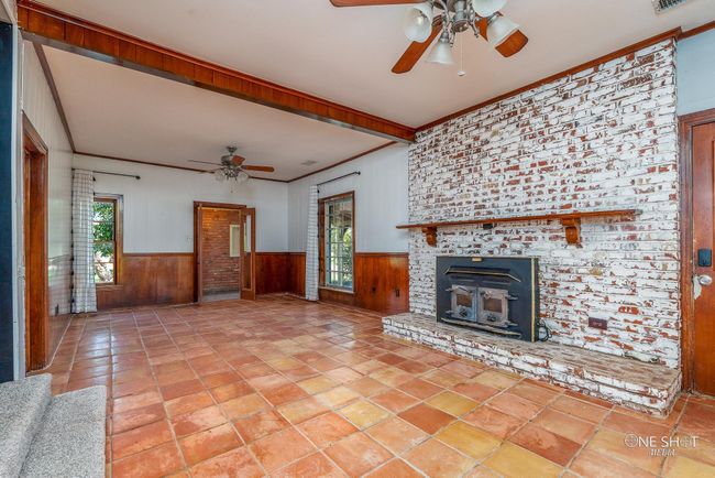 Unfurnished living room featuring wooden walls, ceiling fan, and a brick fireplace | Image 8