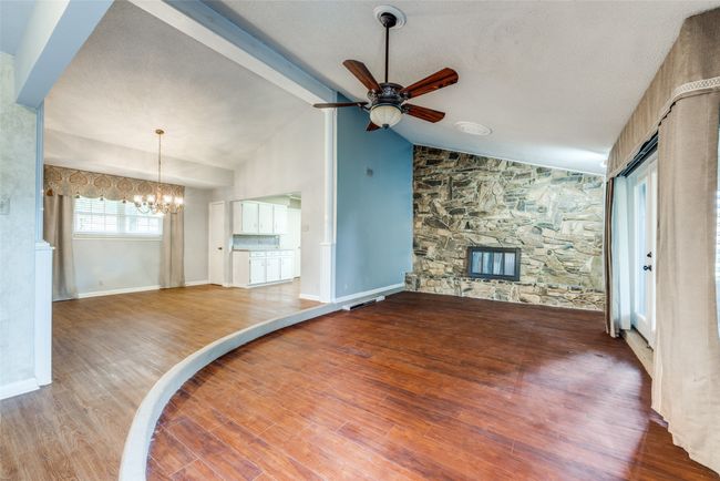 Unfurnished living room with a chandelier, a fireplace, a ceiling fan, wood finished floors, and baseboards | Image 5