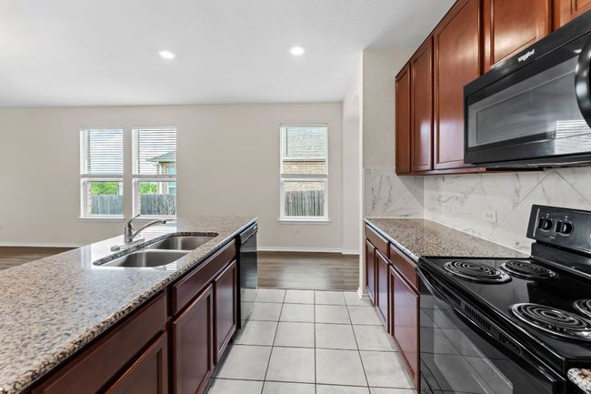Kitchen featuring black appliances, light stone counters, tasteful backsplash, recessed lighting, and light tile patterned floors | Image 9