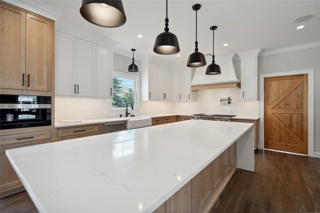 Kitchen featuring custom exhaust hood, dark wood finished floors, appliances with stainless steel finishes, a large island, and white cabinets | Image 13