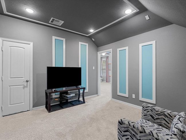This cozy media room features a modern aesthetic with gray walls and blue accents, recessed lighting, and a plush carpet. It leads into the adjoining game room through an open doorway. | Image 36