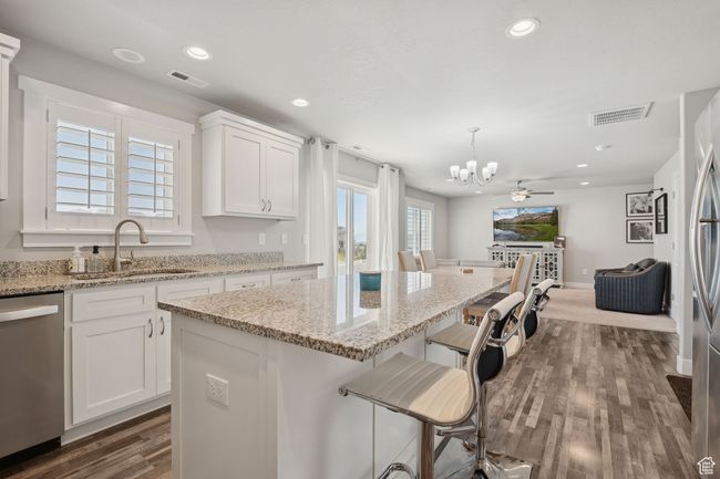Kitchen featuring stainless steel dishwasher, a chandelier, dark wood finished floors, a kitchen island, and white cabinetry | Image 11