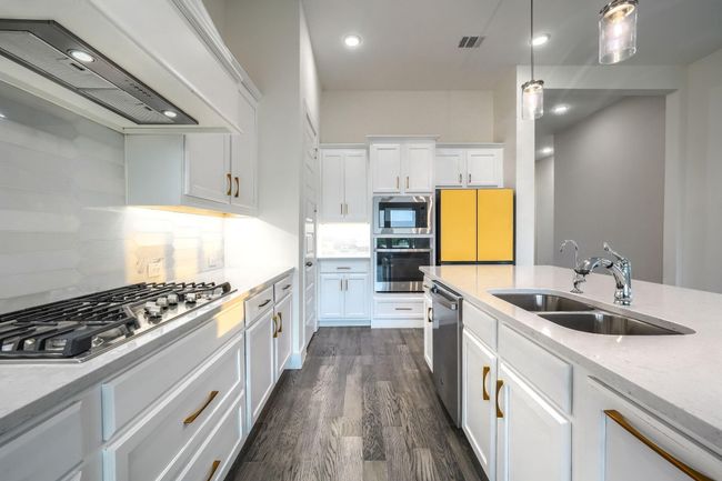 Kitchen featuring stainless steel appliances, wall chimney range hood, a sink, white cabinetry, and backsplash | Image 10