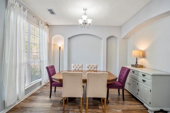 The formal dining room features elegant recessed archways, adding architectural flair to the space. A large window overlooks the front yard, filling the room with natural light and offering a peaceful view. | Image 5