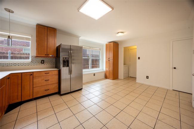 Kitchen featuring light tile patterned flooring, brown cabinets, backsplash, and stainless steel refrigerator with ice dispenser | Image 6