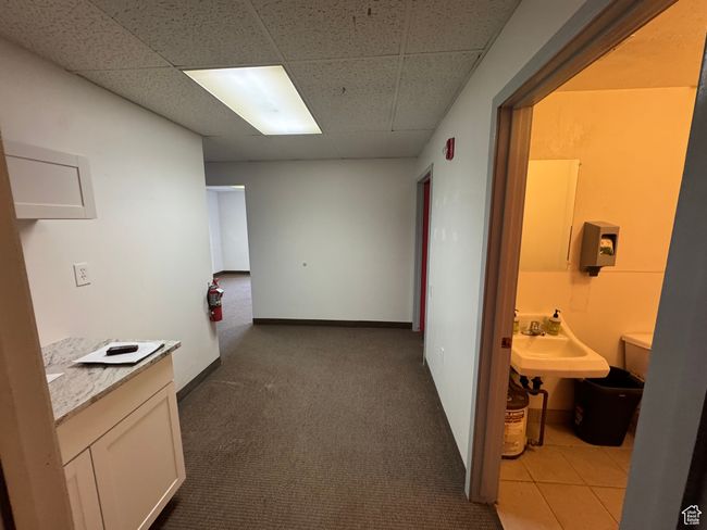 Corridor with carpet flooring, a paneled ceiling, baseboards, and a sink | Image 7