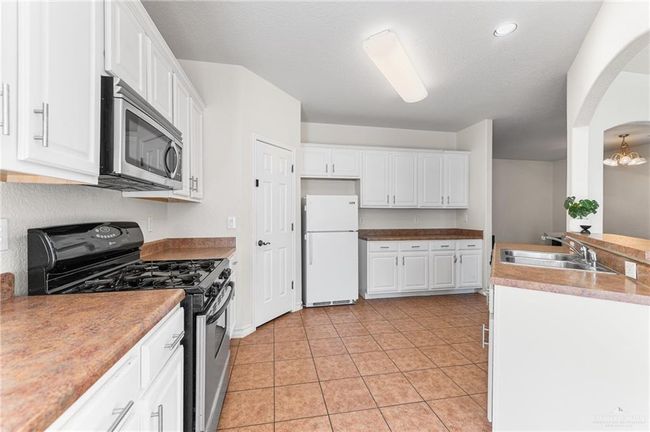 Kitchen featuring range with gas cooktop, freestanding refrigerator, stainless steel microwave, white cabinetry, and light tile patterned floors | Image 21