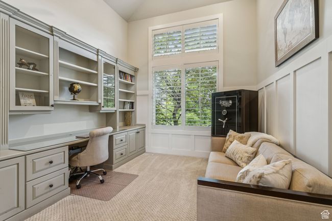Office space with built in desk, a decorative wall, light carpet, lofted ceiling, and wainscoting | Image 25