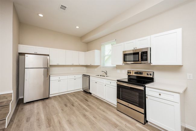 Kitchen featuring stainless steel appliances, white cabinets, light countertops, light wood-type flooring, and recessed lighting | Image 7