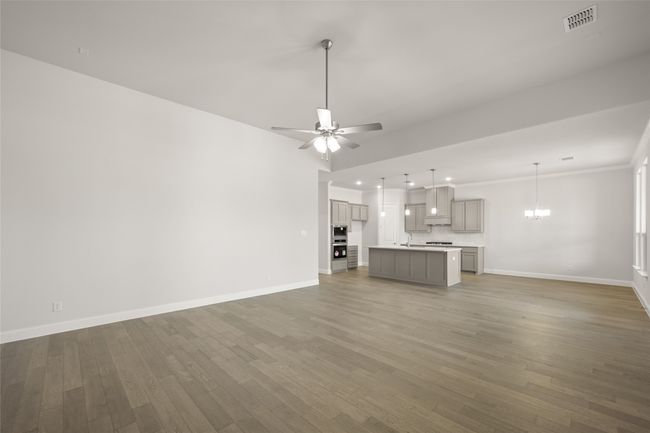 Unfurnished living room with baseboards, wood finished floors, a chandelier, recessed lighting, and crown molding | Image 11