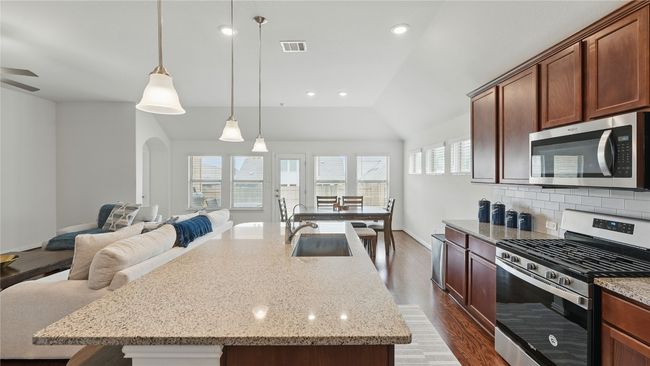 Kitchen with stainless steel appliances, dark wood-style floors, backsplash, open floor plan, and light stone countertops | Image 13