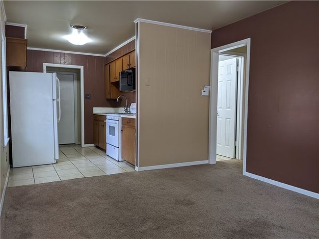 Kitchen featuring white appliances, ornamental molding, light countertops, light carpet, and light tile patterned floors | Image 4