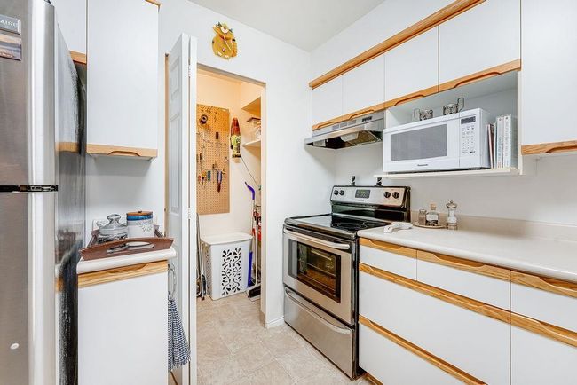 Kitchen with under cabinet range hood, stainless steel appliances, white cabinets, light countertops, and light tile patterned floors | Image 30