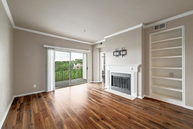 Unfurnished living room with wood-type flooring, built in shelves, a fireplace with flush hearth, and ornamental molding | Image 9