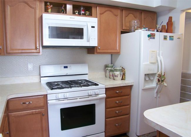 Kitchen with white appliances, light countertops, decorative backsplash, and brown cabinetry | Image 6