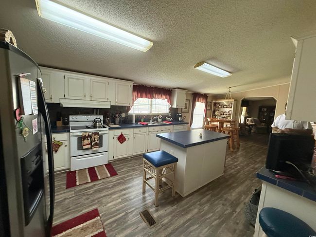 Kitchen featuring electric range, black refrigerator with ice dispenser, under cabinet range hood, a kitchen island, and dark countertops | Image 4