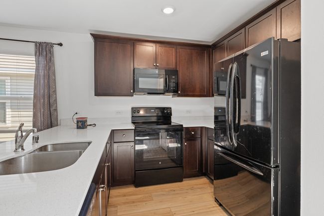 Kitchen featuring light wood-style flooring, dark brown cabinetry, a sink, and black appliances | Image 7