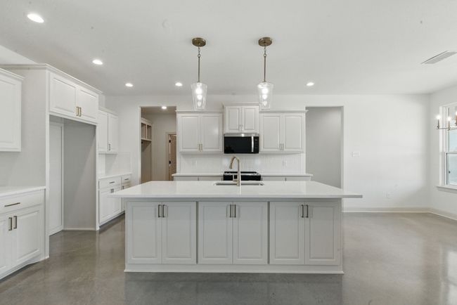 Kitchen featuring finished concrete flooring, stainless steel microwave, decorative backsplash, an island with sink, and a sink | Image 6