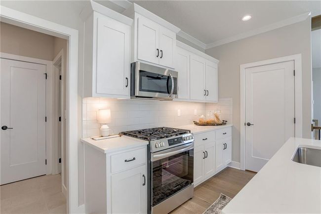 Kitchen with decorative backsplash, light countertops, white cabinetry, and stainless steel appliances | Image 12