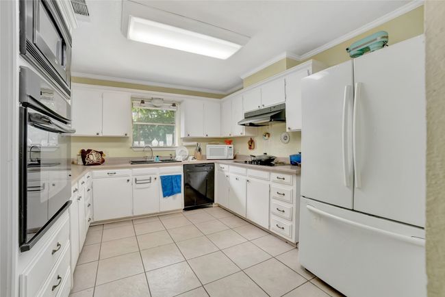 Kitchen with black appliances, under cabinet range hood, ornamental molding, a sink, and light tile patterned flooring | Image 13