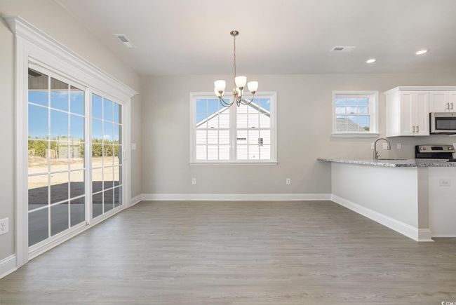 Kitchen featuring light stone counters, stainless steel appliances, pendant lighting, an inviting chandelier, and white cabinets | Image 10
