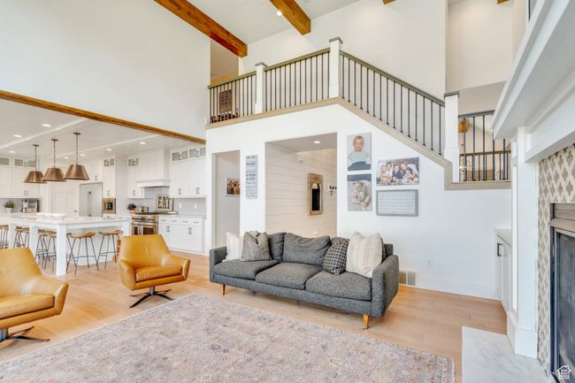 Living area with a towering ceiling, light wood-style floors, a premium fireplace, beamed ceiling, and stairs | Image 16