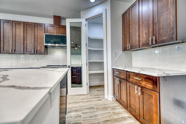 Kitchen with dark brown cabinetry, light hardwood / wood-style flooring, light stone countertops, and backsplash | Image 21