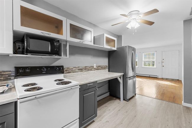 Kitchen with black microwave, gray cabinetry, baseboard heating, freestanding refrigerator, and white range with electric cooktop | Image 9