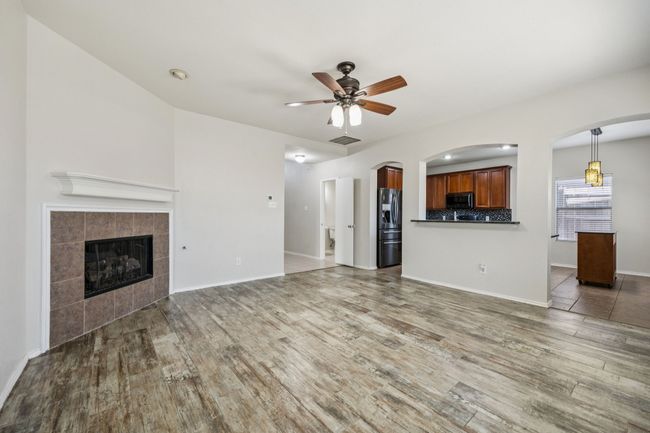 Open floorplan living room featuring wood finished floors, a ceiling fan, a gaslog fireplace, and arched walkways | Image 9
