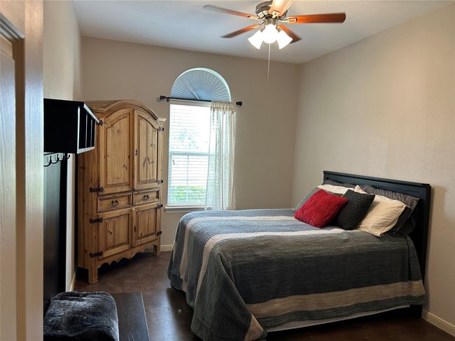 Downstairs secondary bedroom with stained concrete floors & a ceiling fan. There is a full bathroom just outside of the room. | Image 8