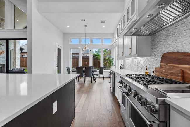 Kitchen with decorative light fixtures, hardwood / wood-style flooring, ventilation hood, a high ceiling, and range | Image 12