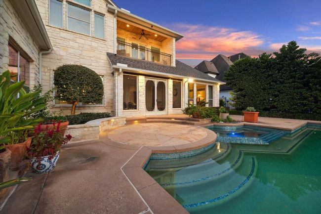 This stunning home features a luxurious outdoor area with a sparkling pool and spa, surrounded by elegant landscaping and a stone patio. The two-story exterior showcases large windows, a balcony, and warm lighting, creating an inviting atmosphere perfect for relaxation and entertaining. | Image 31