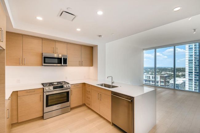 Kitchen featuring stainless steel appliances, a sink, a peninsula, light wood-style floors, and light countertops | Image 9