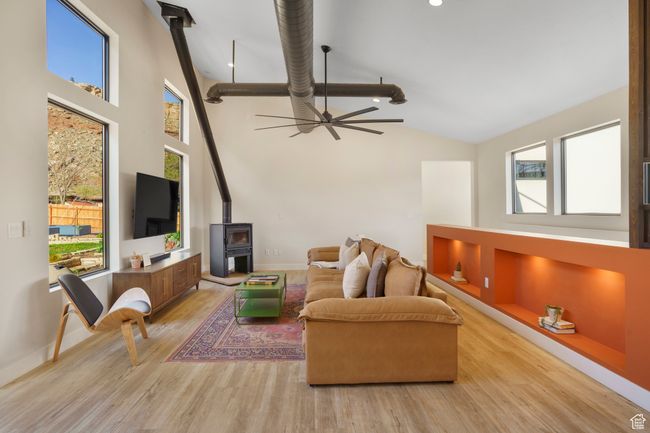 Living room with a wood stove, light wood-type flooring, high vaulted ceiling, baseboards, and a ceiling fan | Image 18