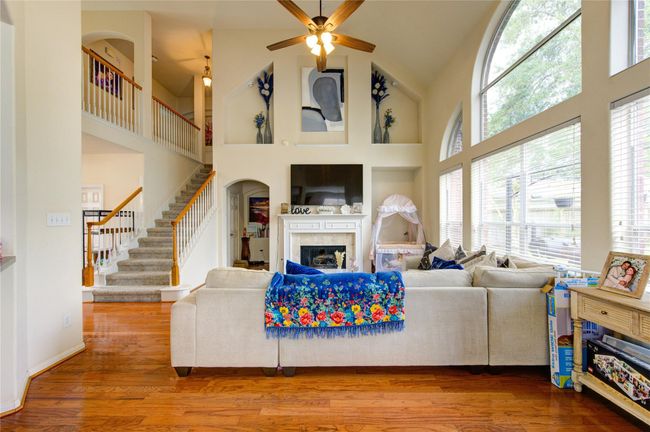 This inviting living room features high ceilings, large arched windows for natural light, and a cozy fireplace. The open layout includes a staircase with a wooden railing and a spacious seating area with hardwood floors. Ideal for family gatherings and entertaining. | Image 20